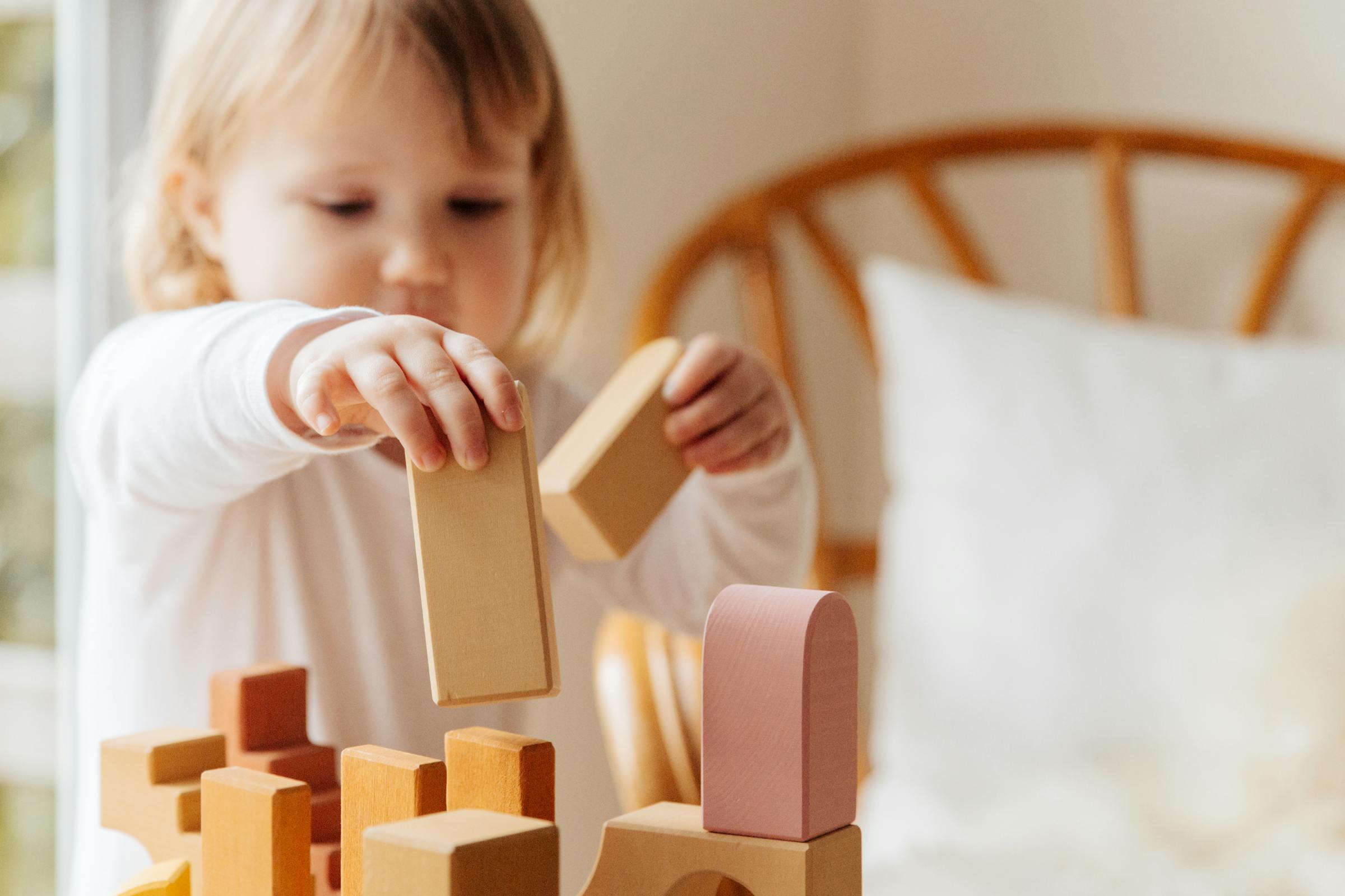 Petite fille jouant avec des blocs en bois Montessori dans une piece baignee de lumiere naturelle